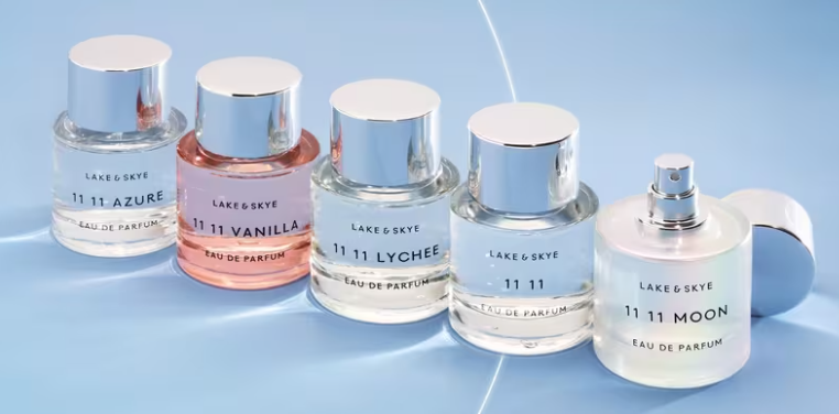 A row of Lake & Skye 11 11 eau de parfum bottles, including Azure, Vanilla, Lychee and Moon, on a pale blue surface.