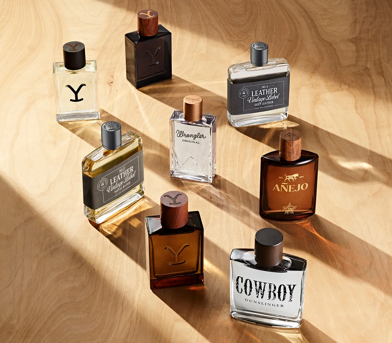 Tru Western colognes, among them Yellowstone, Leather Vintage Label, Wrangler, Añejo and Cowboy Gunslinger, on a sunlit wooden surface.